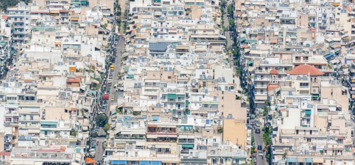 Aerial view of a dense urban neighborhood with closely packed white and beige buildings and narrow grid-like streets.