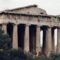 Ancient ruined temple with tall stone columns and carved frieze, visitors at the base among bushes.