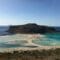Rocky, flat-topped island with a sandy beach and turquoise shallow waters, boats anchored offshore nearby.