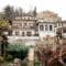 H hillside village inn with white plaster walls, stone accents and a wooden balcony, set among leafless trees and a garden.
