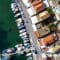 Aerial view of a harbor with boats docked along a quay and a town with orange-tiled roofs beside turquoise water.