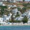 Whitewashed hillside town with blue doors and windows, terraced gardens, and a sandy beach by turquoise sea.