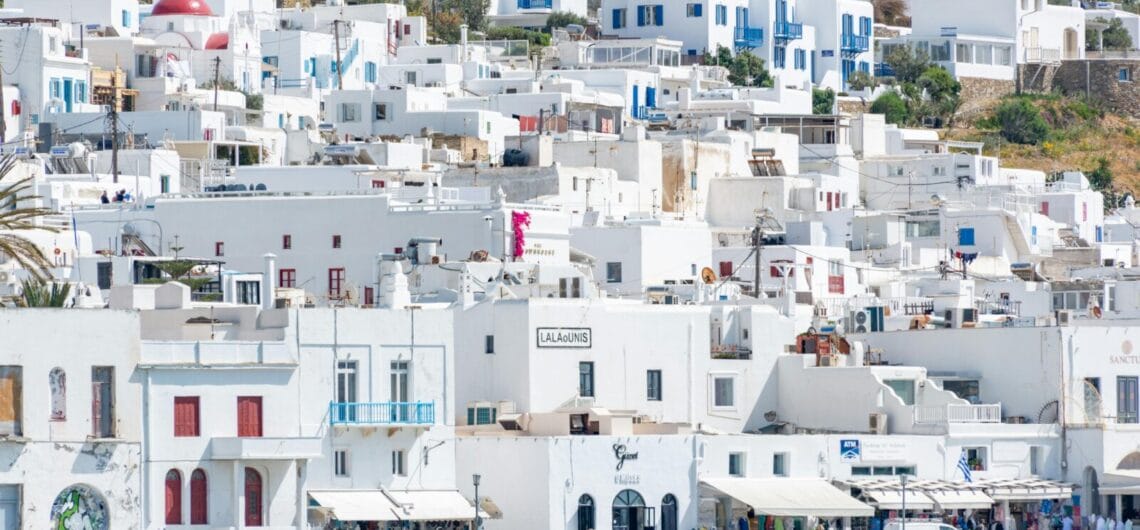White-washed buildings with blue doors and balconies along a coastal waterfront area.