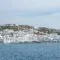 White-washed buildings cascade down a hillside to a calm blue sea under a pale sky, coastal town by the water.