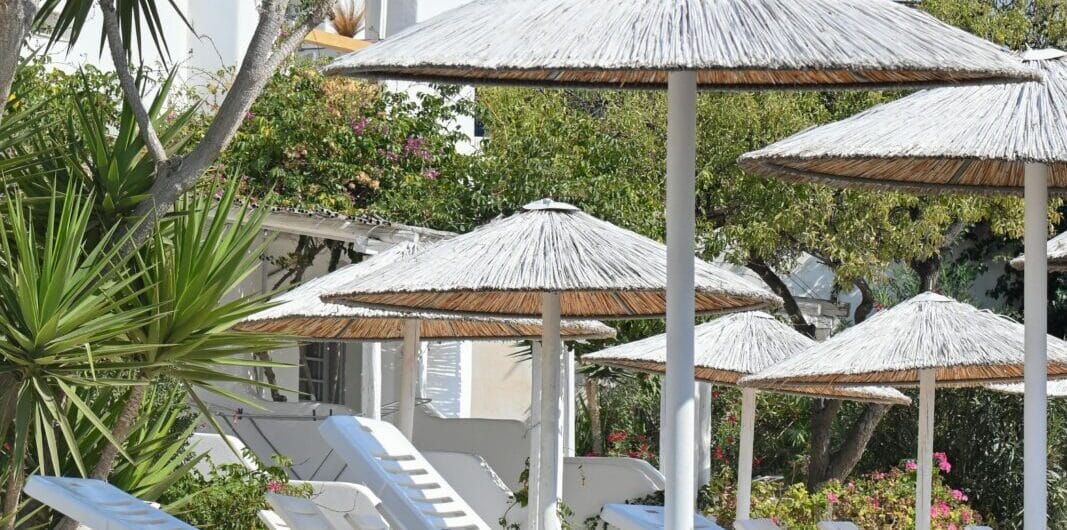Rows of white lounge chairs under thatched umbrellas at a sunny beach resort. AI