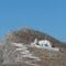 Whitewashed church with domes and a bell tower perched on a rocky hillside, with white-washed steps climbing the slope beneath a blue sky