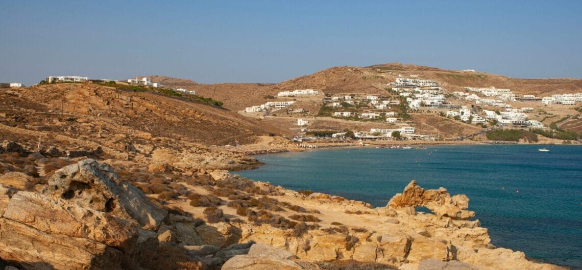 Rocky coastline slopes down to a blue bay, with white-washed houses dotting the hillside.