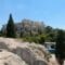 Ancient Parthenon ruins atop a rocky hill with surrounding trees under a clear blue sky.