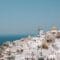 Whitewashed Cycladic buildings with domed roofs cascading down a cliff toward the blue sea and sky, Santorini, Greece.