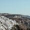 White-washed buildings cling to a cliffside town overlooking the blue sea and distant cliffs.