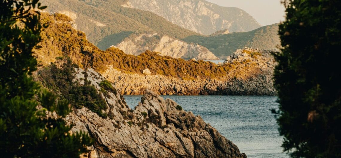 Coastal cove with rocky shoreline, calm water, and green trees framing the scene; a yellow boat floats near the shore.